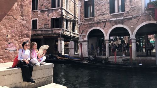 Female friends sitting by canal in city