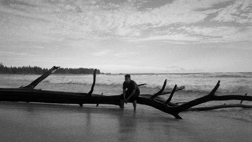 Man sitting on fallen tree trunk at shore