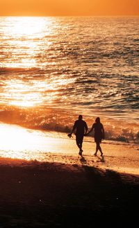 Silhouette people on beach against sky during sunset