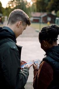 Teenage male and female friends using app on smart phones while standing on street