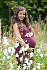 Portrait of smiling pregnant woman with hands on stomach standing in park