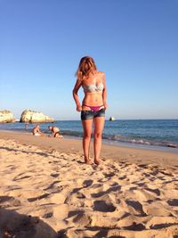 Woman wearing hot pants standing on shore at beach against sky