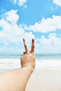 Midsection of person hand on sea shore against sky