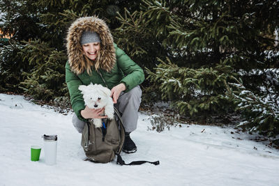 Pet care in winter cold season. happy woman and maltese dog in backpack walking, having fun and