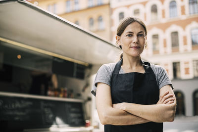 Front view of confident female chef standing by food truck in city