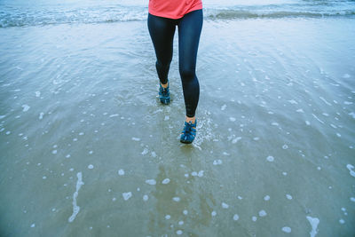 Low section of woman running at beach