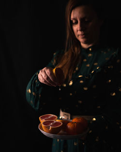 Midsection of woman a grapefruit's plate against black background