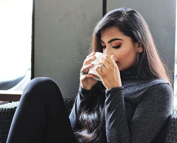 Young woman drinking coffee while sitting on sofa