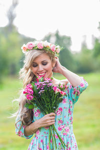 Happy woman with pink flower standing against plants