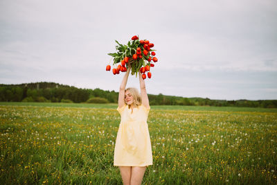 Smiling charming female with bouquet of red tulip flowers sitting in green meadow in summer
