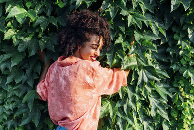 Happy woman with eyes closed embracing green leaves on sunny day