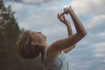 Side view of beautiful woman dancing against cloudy sky