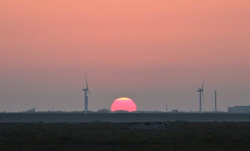 Sunset behind a windmill,  with half os the red  sun under ground. 