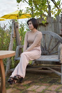 Full length of young woman sitting on seat against trees