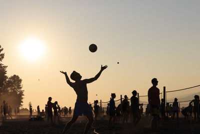 Silhouette people playing volleyball at beach during sunset