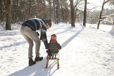 Father teaching sledding to son on snow during sunny day