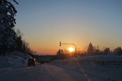 Road by snow covered street against sky during sunset