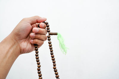 Cropped hand holding prayer beads over gray background