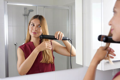 Close up of young woman latin using steam straightener to style hair in the mirror on bathroom