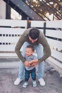 Dad tickling baby boy in front of white fence