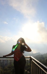 Rear view of woman standing by railing against sky