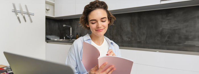 Portrait of young woman using mobile phone while standing in office