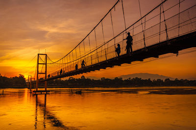 Silhouette bridge over river against sky during sunset