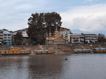 Buildings by river against sky in city