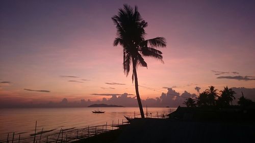 Low angle view of silhouette coconut palm tree by sea against sky at dusk