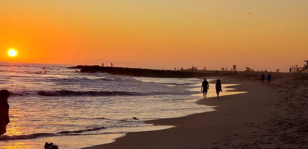 Silhouette people on beach against sky during sunset