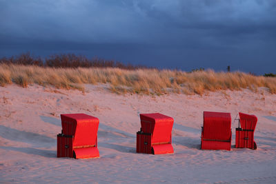Red hooded beach chairs on sand on field against sky
