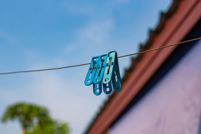 Low angle view of clothespins hanging on rope against blue sky