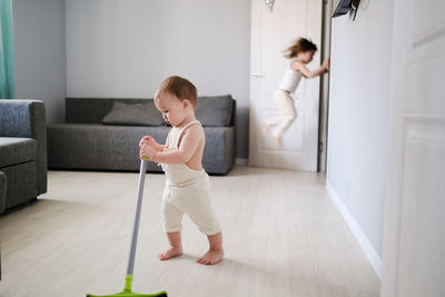 Children siblings with mop sweep floor in bright living room, help with housework 