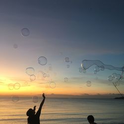 Silhouette people at beach against sky during sunset