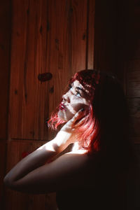 Sunlight falling on young woman standing by wall at home