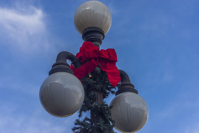 Low angle view of red ribbon tied up on street light against sky