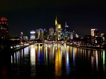 Illuminated buildings by river against sky at night