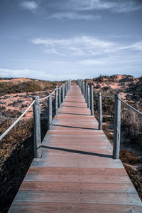 View of wooden bridge over water against sky