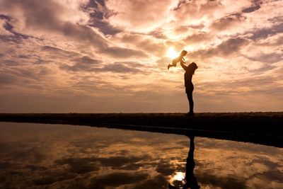 Low angle view of woman with baby by lake against cloudy sky during sunset