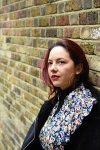 Portrait of young woman standing against brick wall