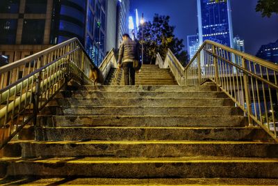 Rear view of man walking on steps in city at night