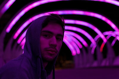 Close-up portrait of young man against illuminated purple lighting