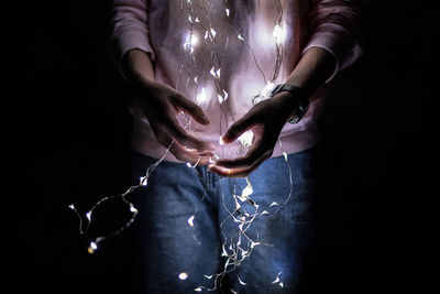 Close-up of hand holding illuminated lighting equipment against black background