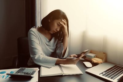 Stressed businesswoman using smart phone at desk in office