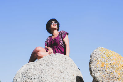 Low angle view of young woman standing against clear blue sky