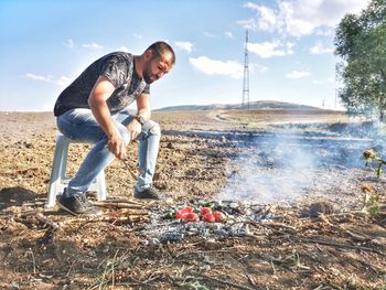 Full length of man roasting tomatoes on campfire