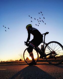 Silhouette man riding bicycle on street against sky