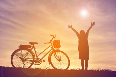 Silhouette boy standing by bicycle against sky during sunset