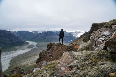 Man standing on cliff looking at mountains against sky