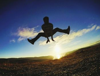 Low angle view of man jumping against sky during sunset